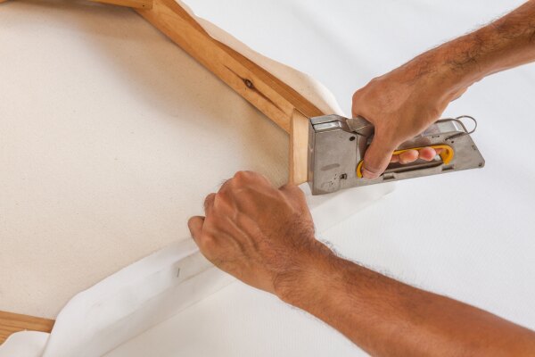 Hands stapling canvas onto wooden stretcher bars